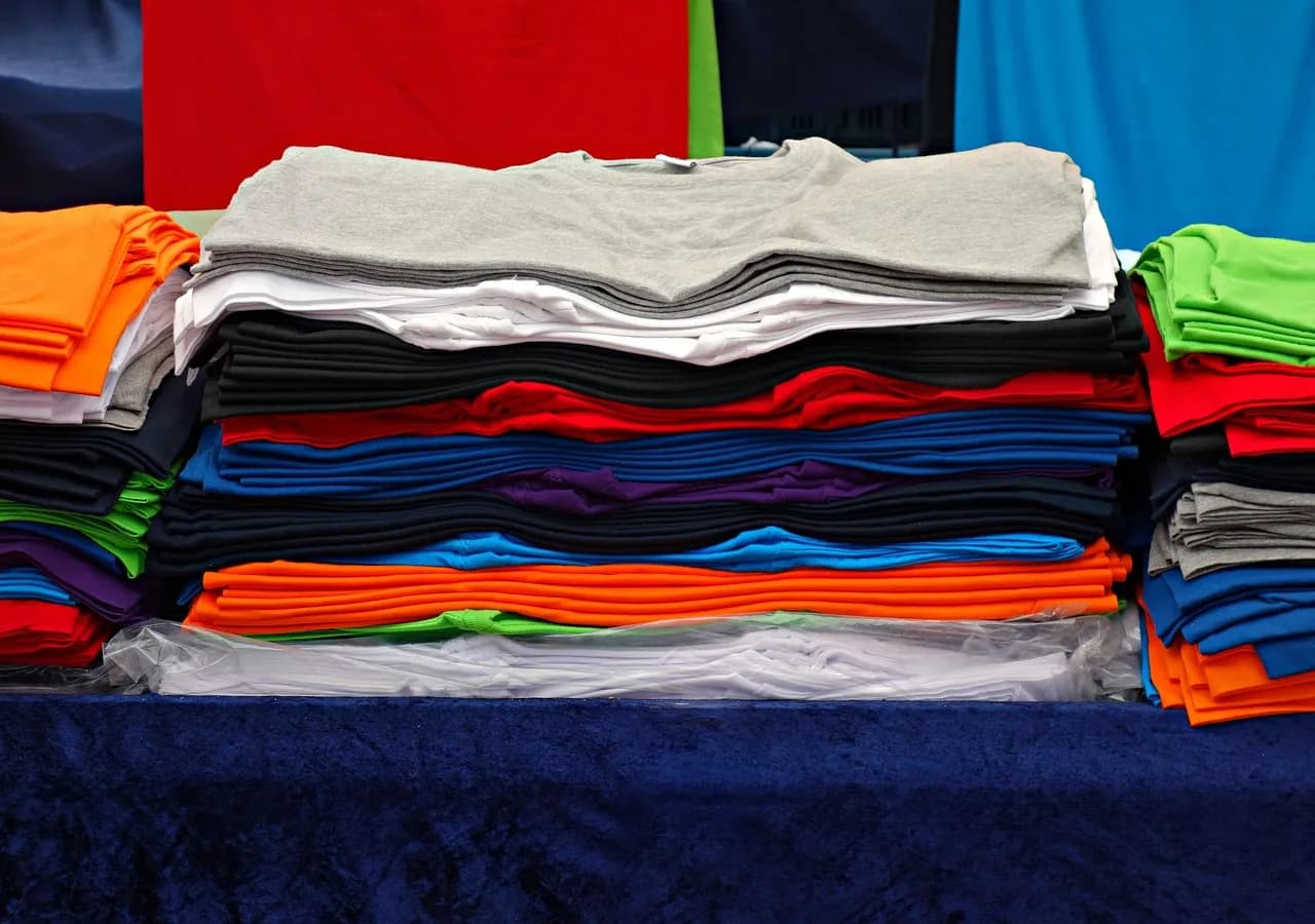 Stacks of folded plain t-shirts in assorted colours, ready for bulk branding